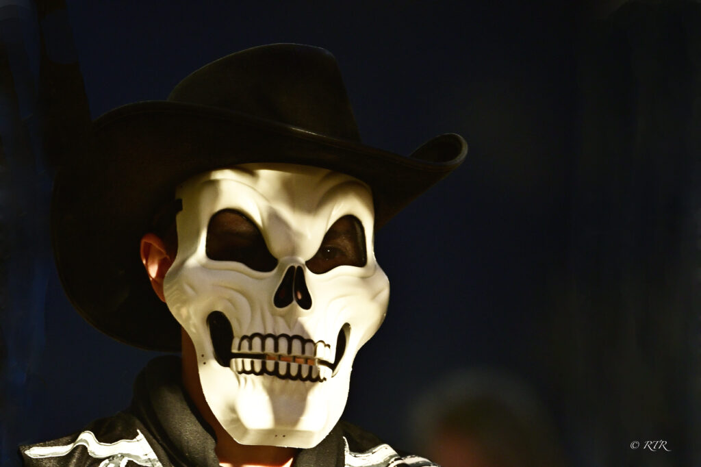 A person in a skeleton mask and black cowboy hat, photographed by Ronny Rooster.